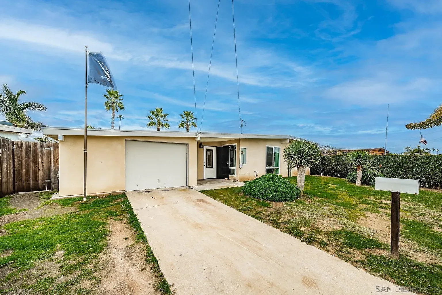A single-story house with a garage, grassy area, palm trees