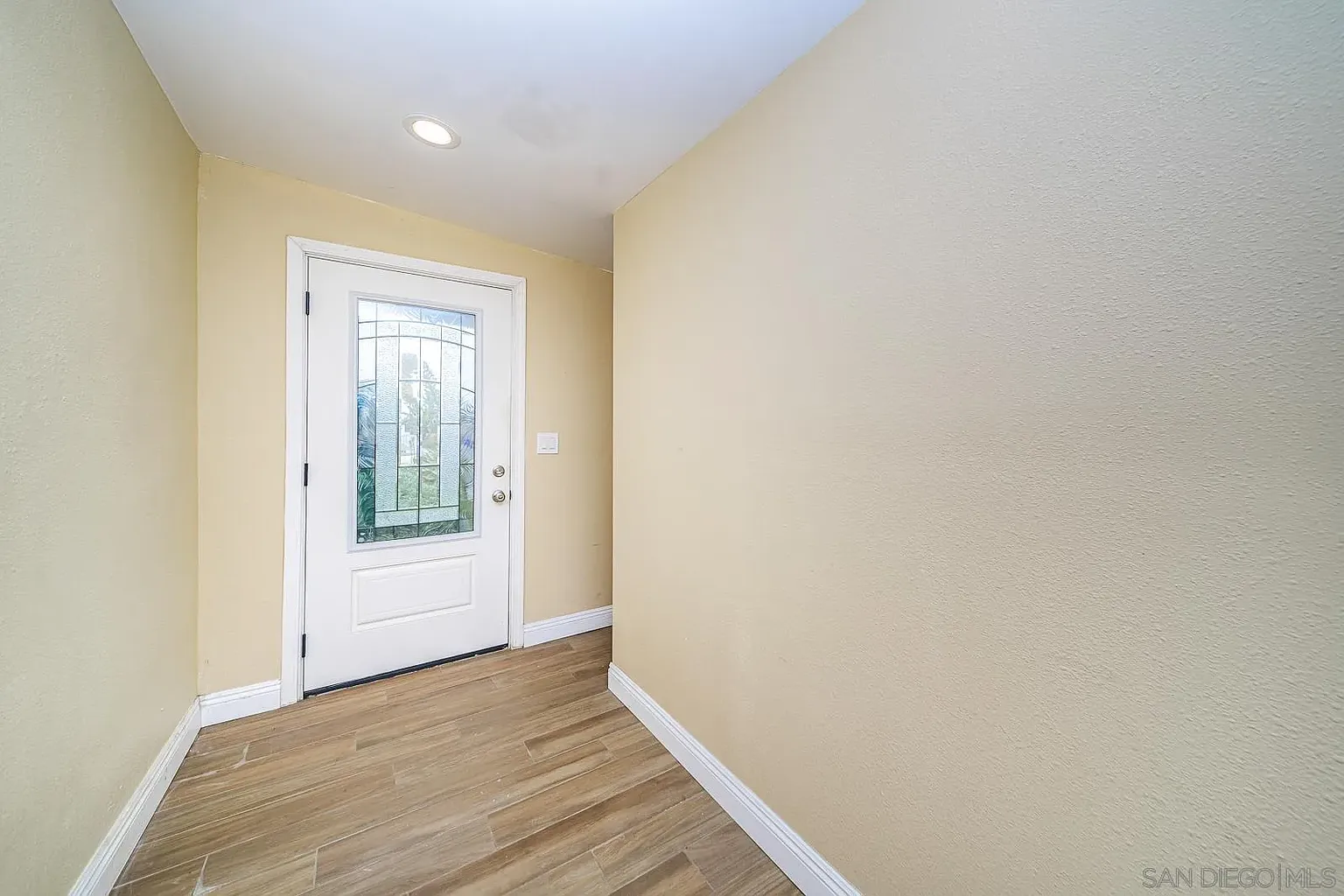 A hallway with light-colored walls leading to a front door with a decorative glass panel.