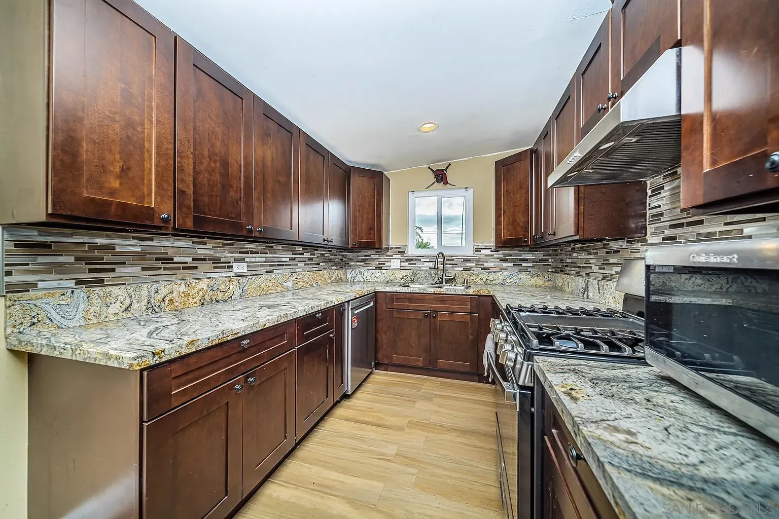 Kitchen with dark wood cabinets, granite counter, stainless sink, oven, and tile backsplash.