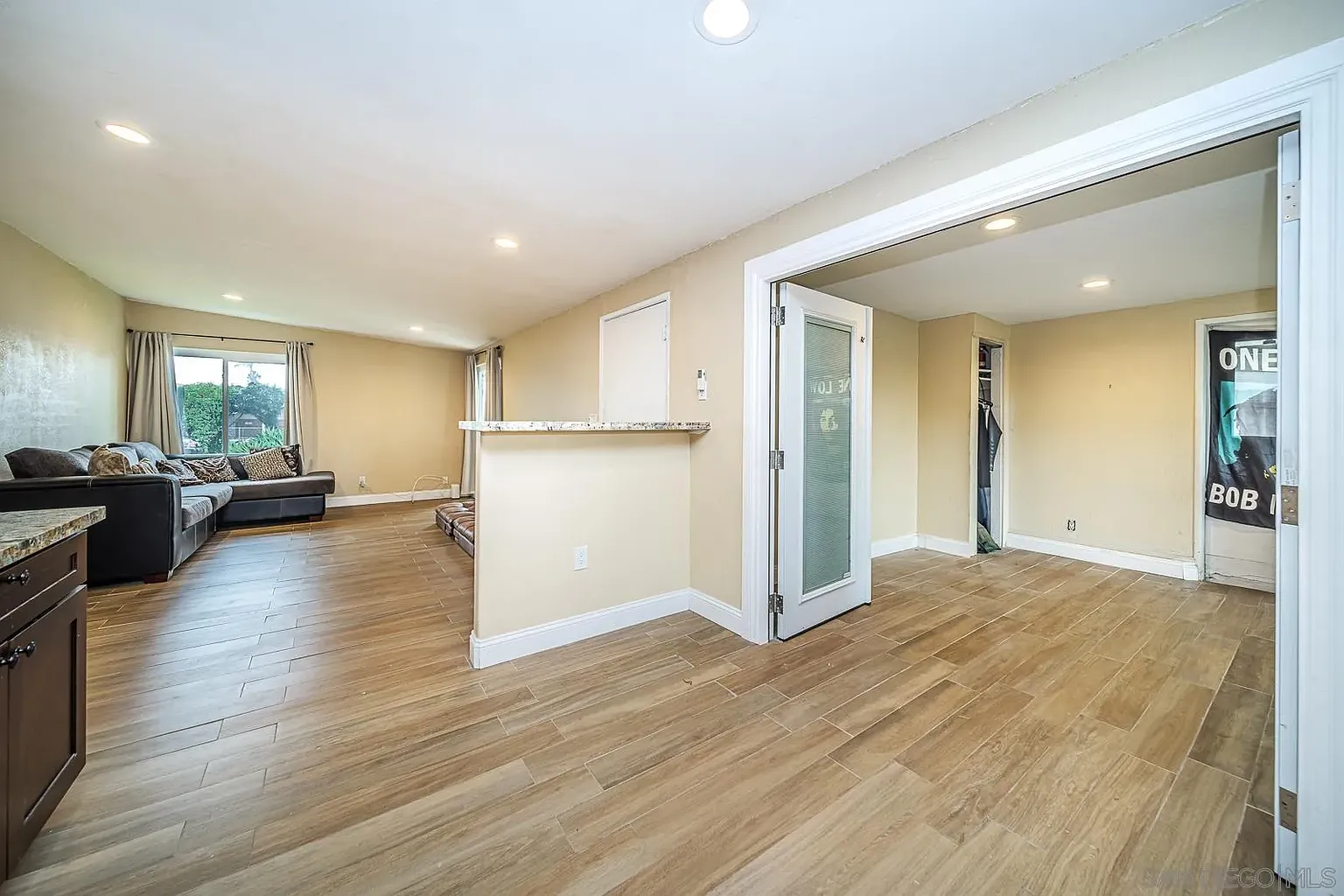 Living room with beige walls, wood floor, large window, couch, and open doorway.
