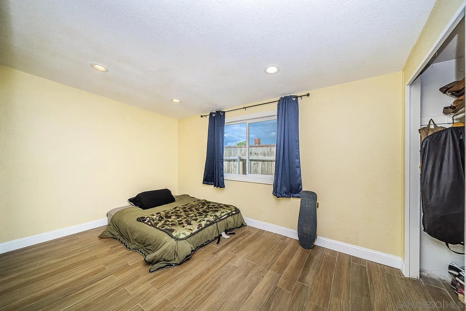 Room with yellow walls, bed with dark blanket, window with curtains, and skateboard.