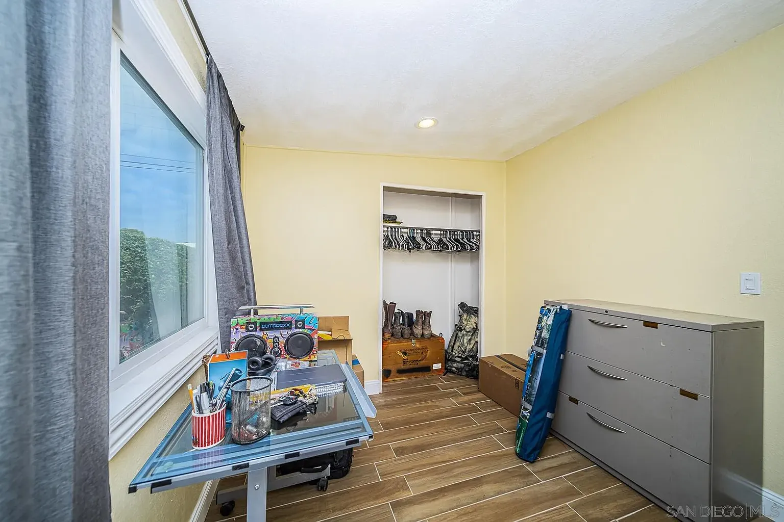Room with yellow walls, large window, desk with items, and closet shelves.