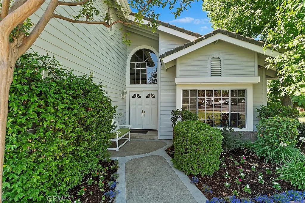 Luxury house California real estate with gray exterior, arched window, hedges, and flowers.