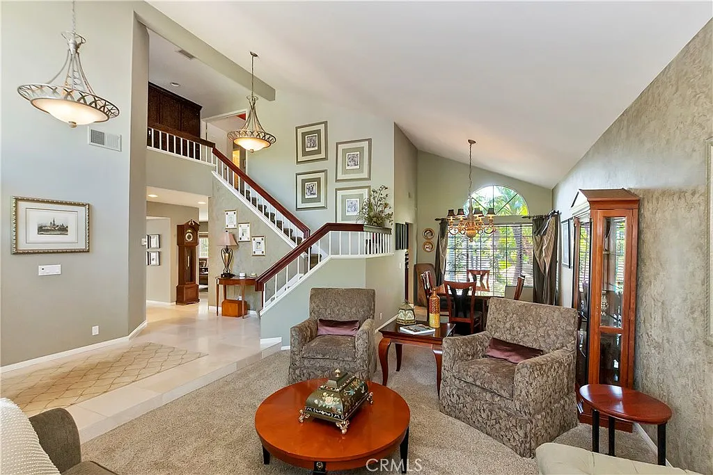 Living room with patterned armchairs, round wooden coffee table, staircase, and decorative artwork on walls