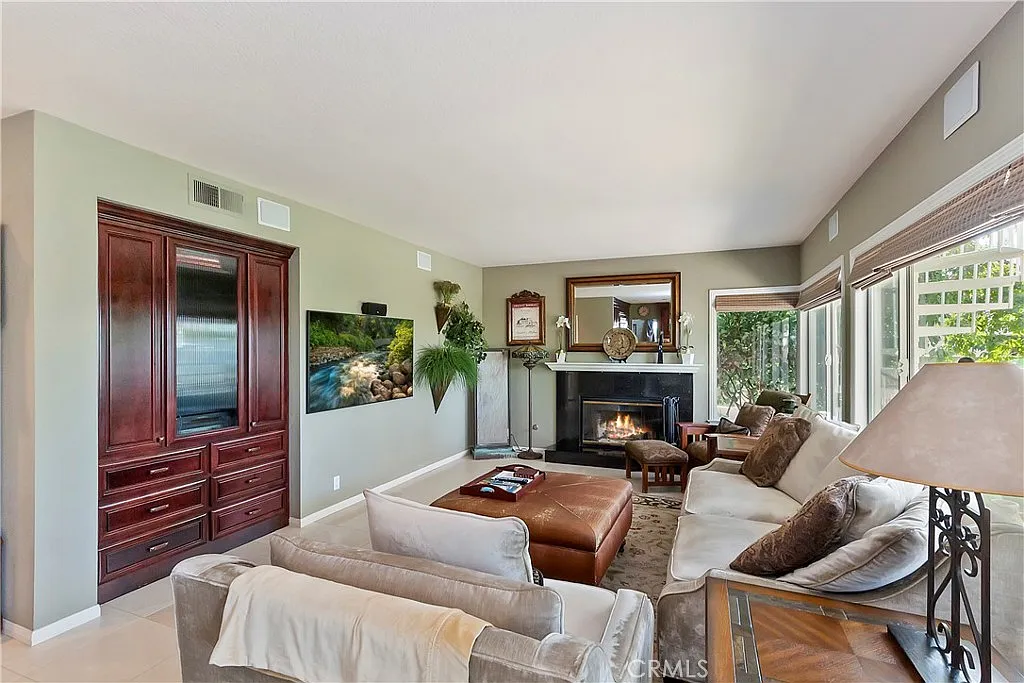 Living room with sofa, ottoman, fireplace, wooden entertainment unit, and plants