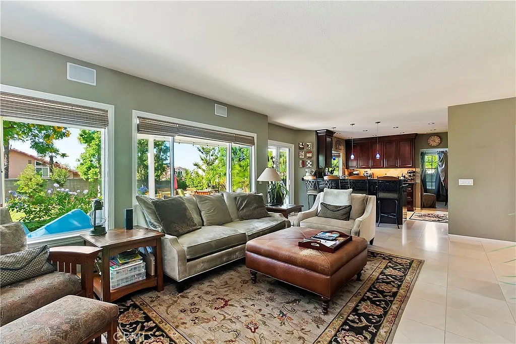 living room with beige couch, leather ottoman, coffee table, patterned rug, and kitchen with dark cabinets in background