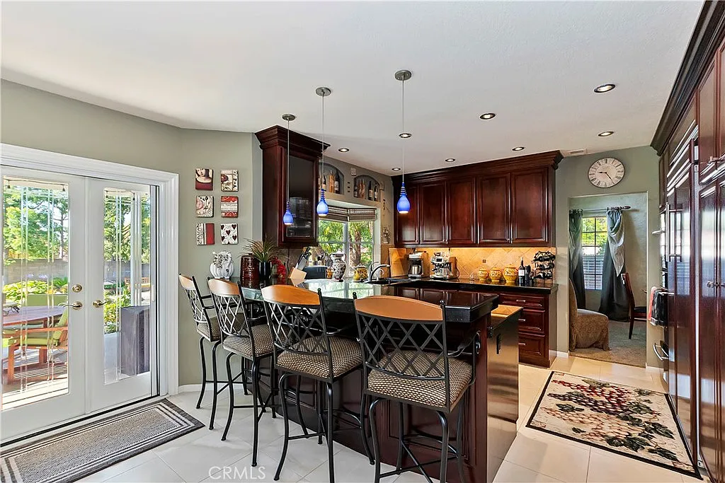 Kitchen with dark wood cabinets, stainless steel appliances, breakfast bar with stools, and dining area visible through glass doors