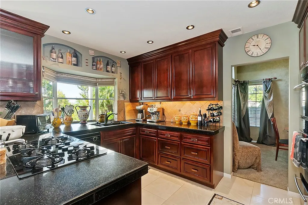 Kitchen with dark wood cabinets, granite countertops, gas stove, and decorative items on shelves