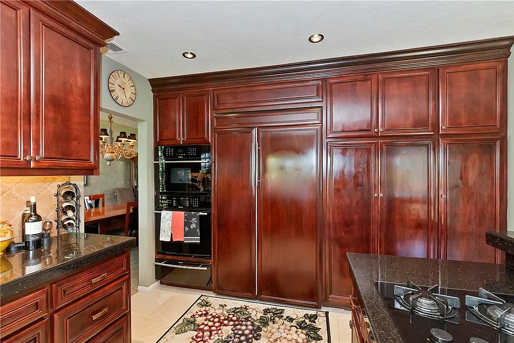 Kitchen with dark wood cabinets, black appliances, large refrigerator, gas stove countertop, and fruit-design rug