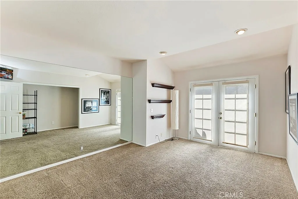 room with carpet, large mirrored wall, double French doors, shelving units, and framed pictures on walls