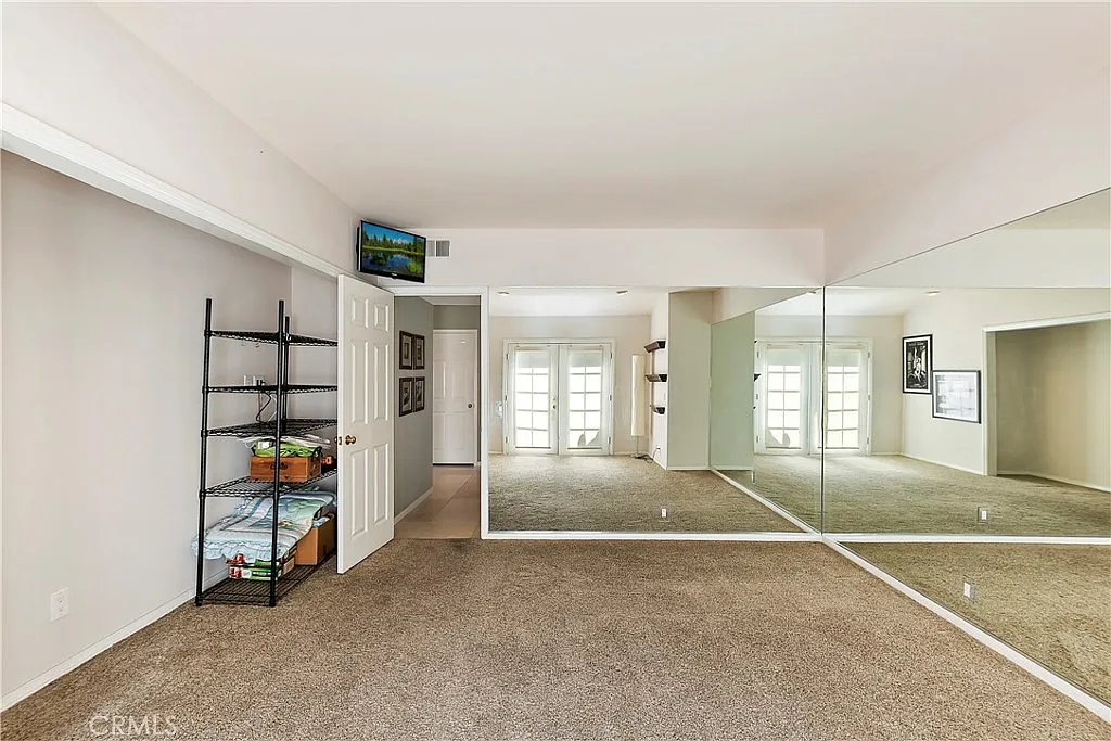 room with beige carpet, mirrored wall, light-colored walls, shelf with items, door to another room, and natural light from windows