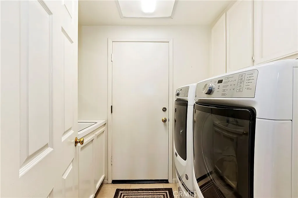Laundry room with washer and dryer, white cabinets, door to another area, and small floor rug