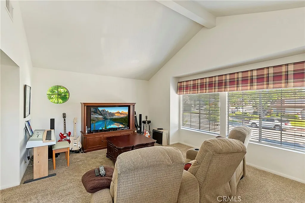 living room with large TV on wooden stand, two recliners, keyboard, and windows with plaid curtains letting in natural light