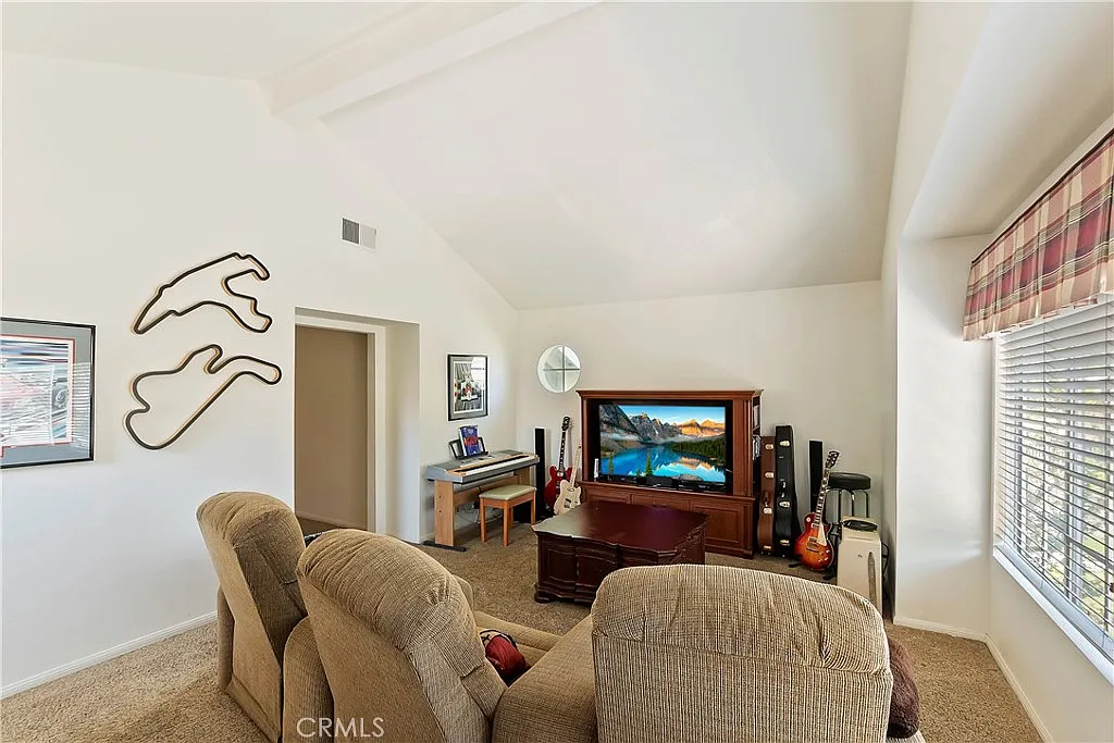 living room with sectional sofa, wooden entertainment center with TV and decorations, large windows with blinds, wall art, and corner guitars