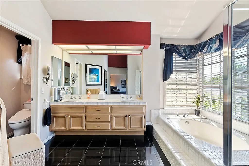 Bathroom with wood double vanity, large mirrors, tub by window, and glass shower.