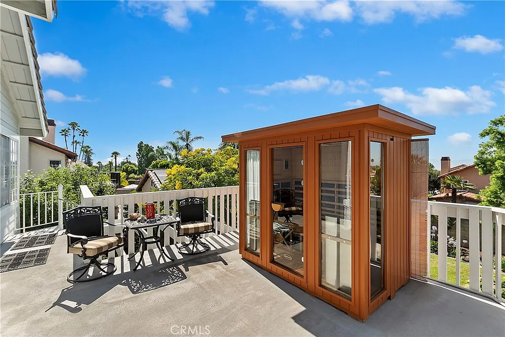 Wooden outdoor shed on balcony with gray flooring, small table and chairs, and green trees