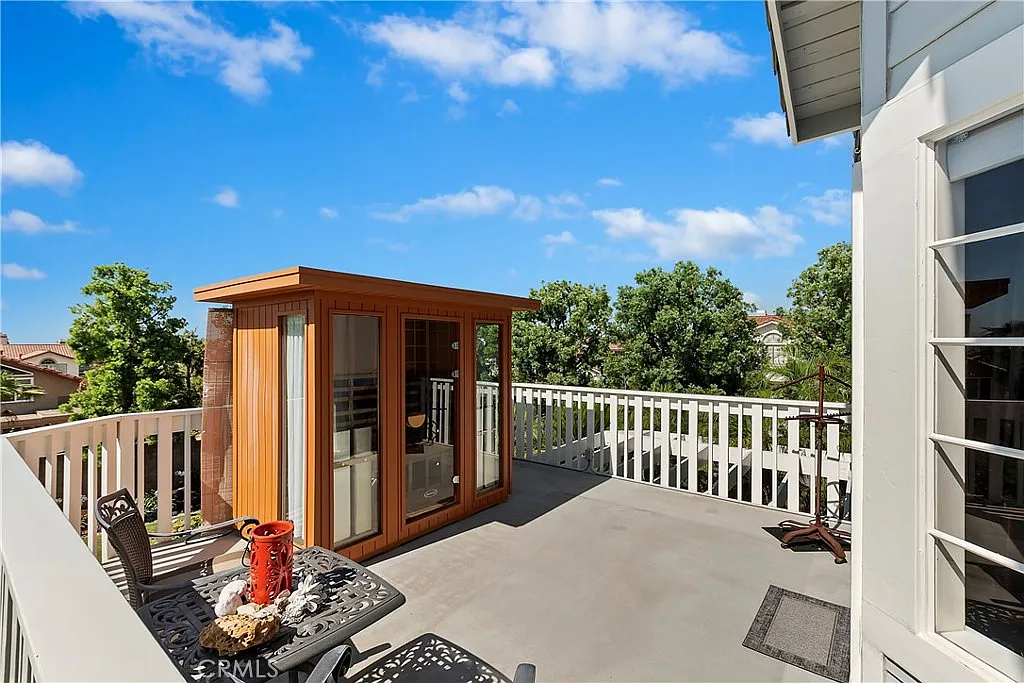 Wooden outdoor shed on balcony with gray flooring, small table and chairs, and green trees
