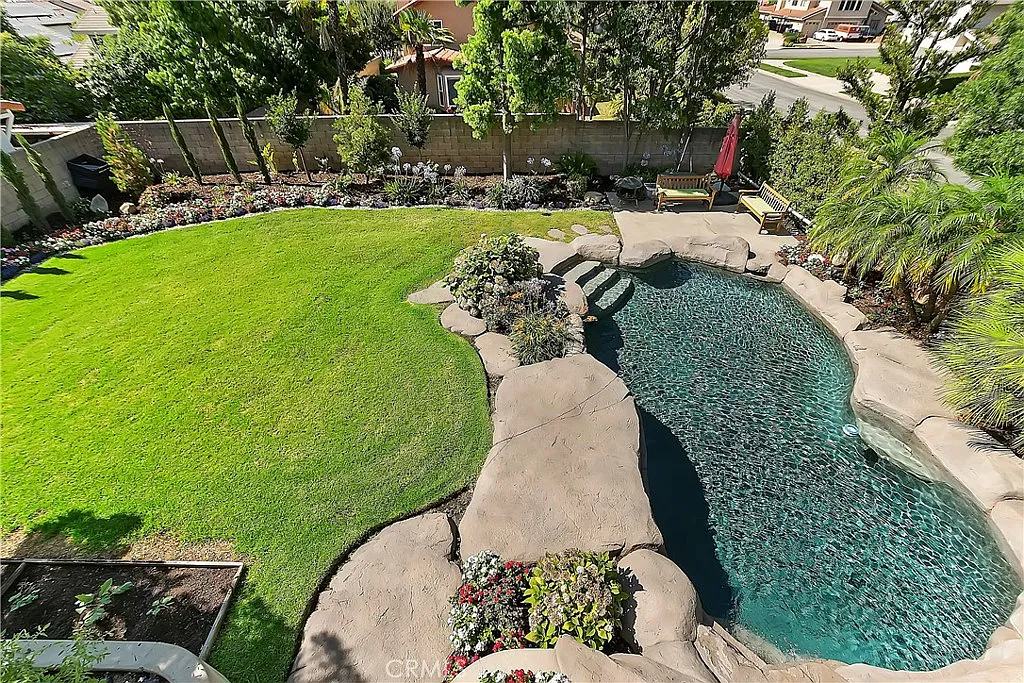 Aerial view of landscaped backyard with swimming pool, green lawn, and surrounding plants and flowers
