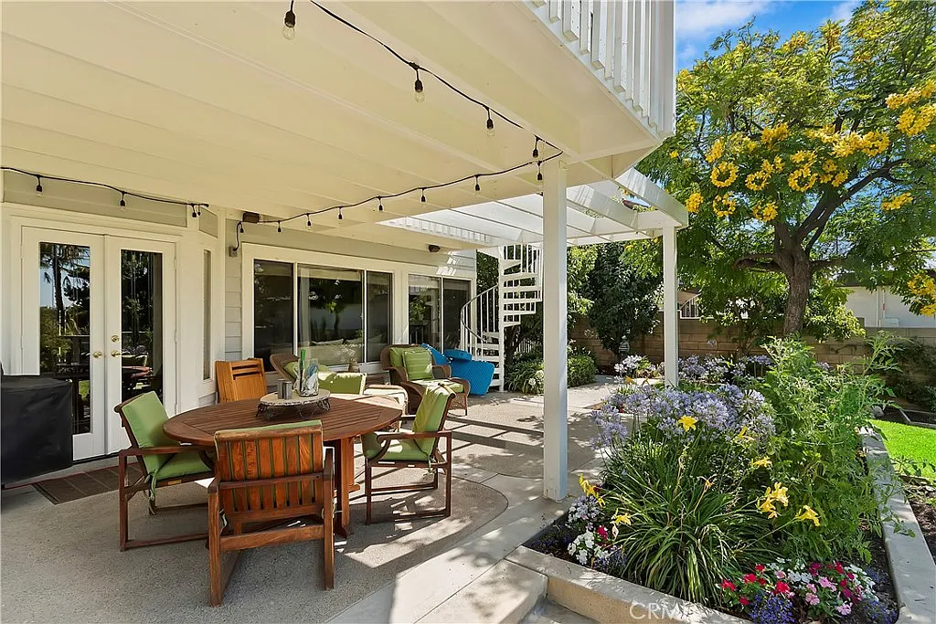 Backyard patio with wood table, chairs, grill, string lights, and plants.