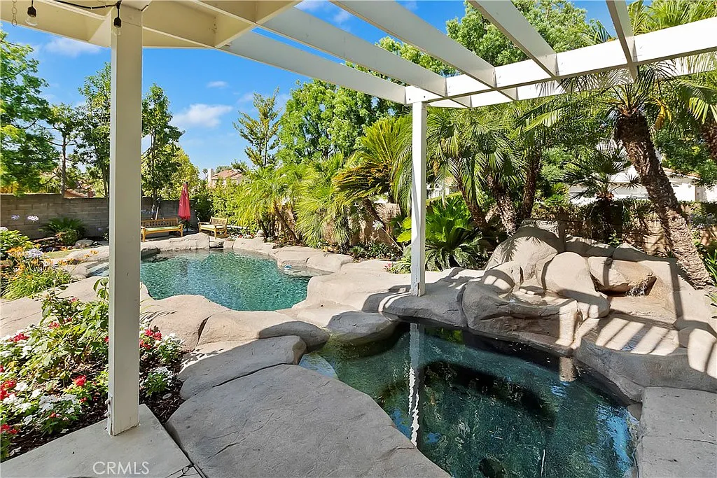 Backyard with two pools, tropical plants, green landscaping, and outdoor shade structure.