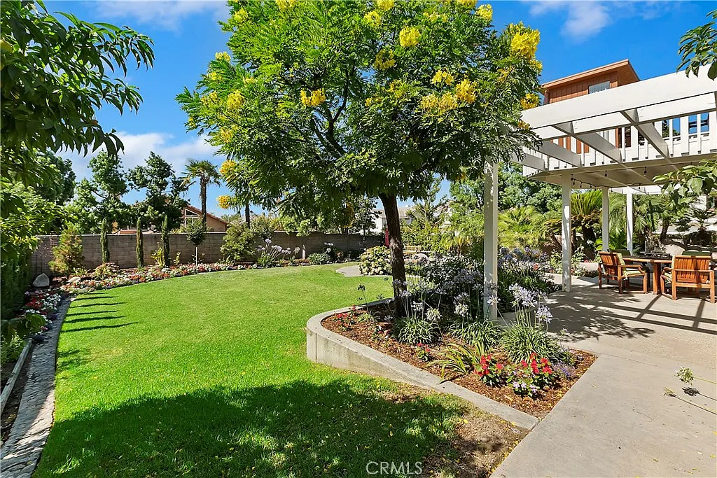 Spacious backyard with lawn, flower beds, patio with dining furniture, and trees and shrubs