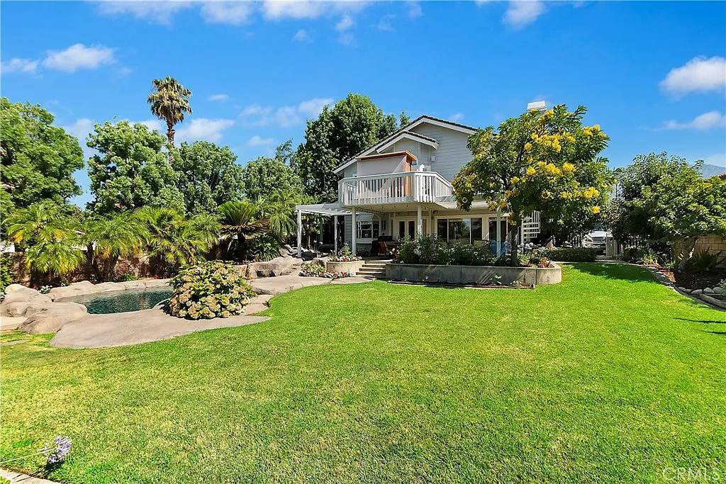 House with well-maintained garden, colorful flower beds, palm trees, and greenery
