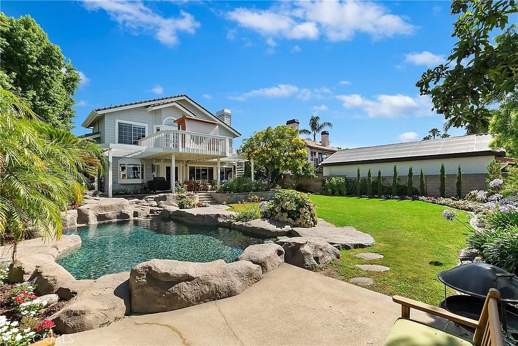 Spacious backyard with swimming pool, rocks, greenery, and large house