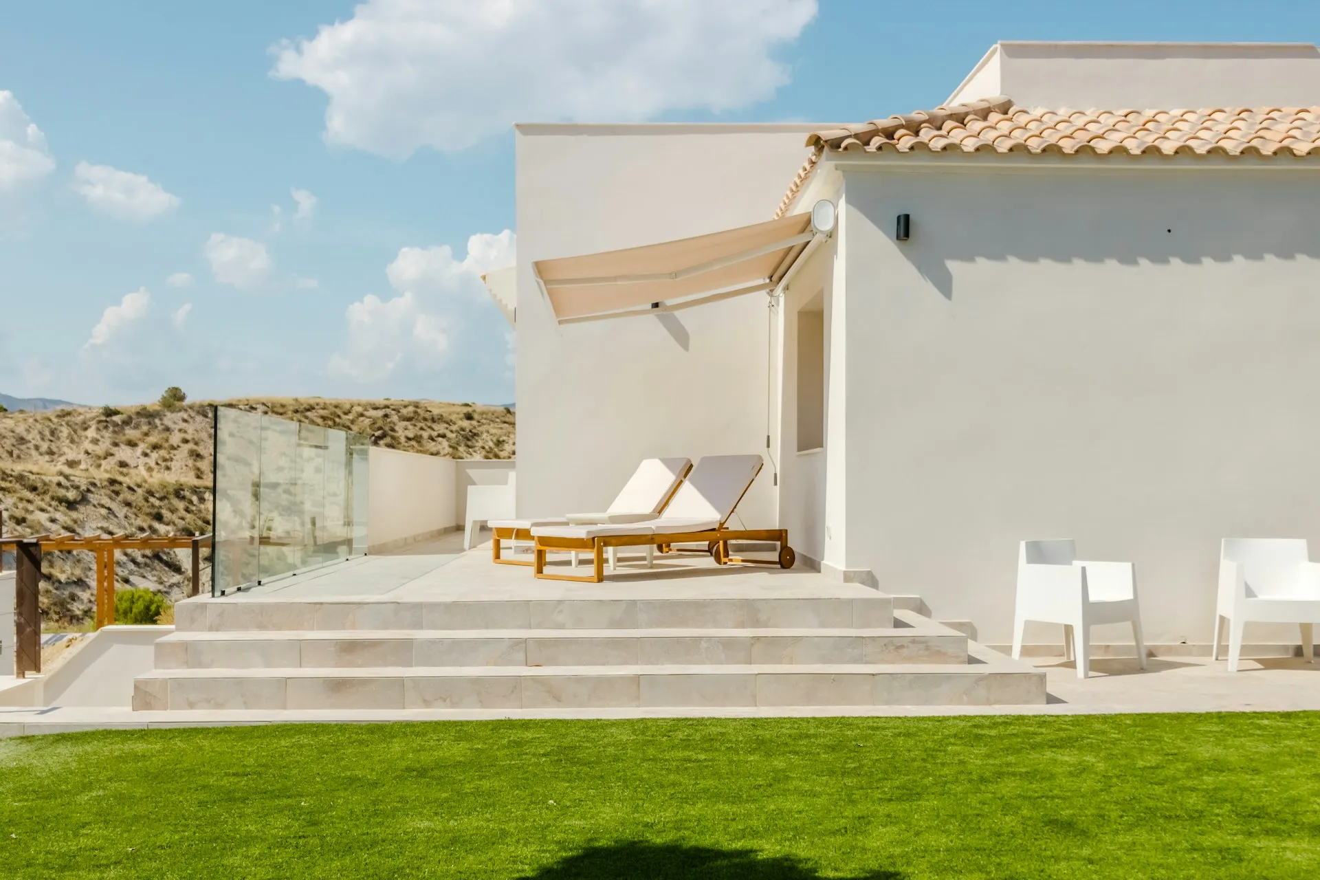 A white building with steps, a grassy yard, and a sun lounger outside.