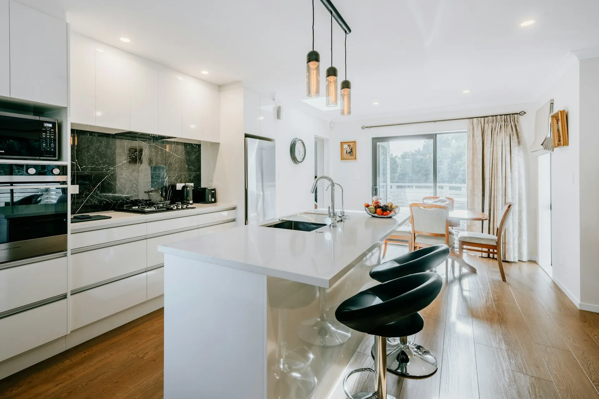 A kitchen with white cabinets, black marble backsplash, island with bar stools, and a dining area.