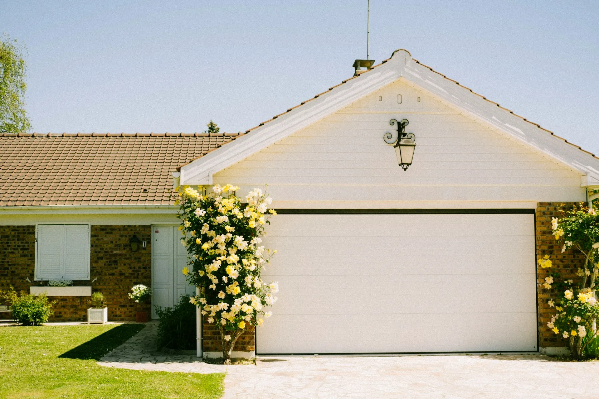 White house with tiled roof, garage door, and yellow rose bushes along the sides, California real estate.