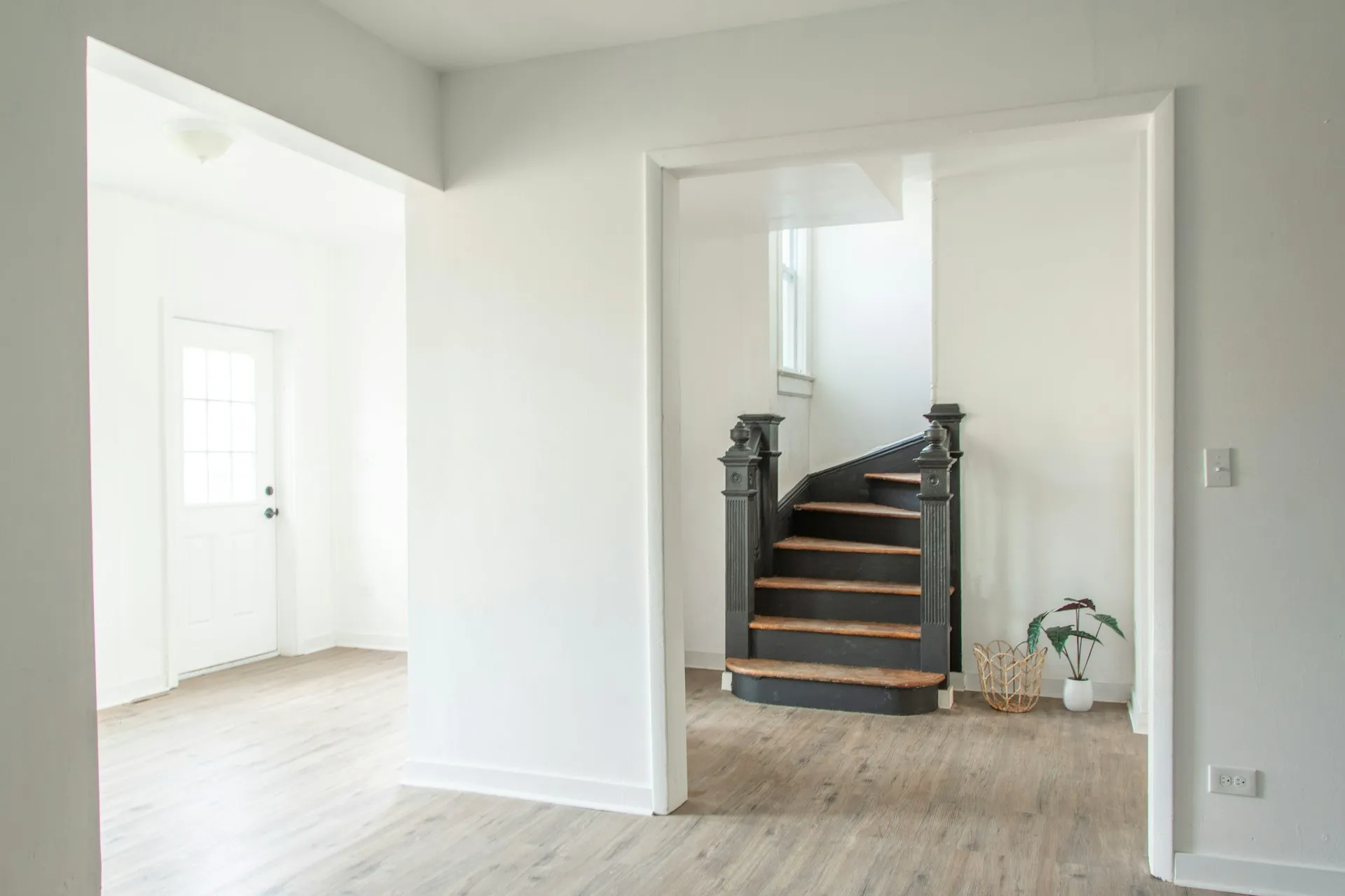 A bright room with dark wood stairs, white walls, and a door leading outside.