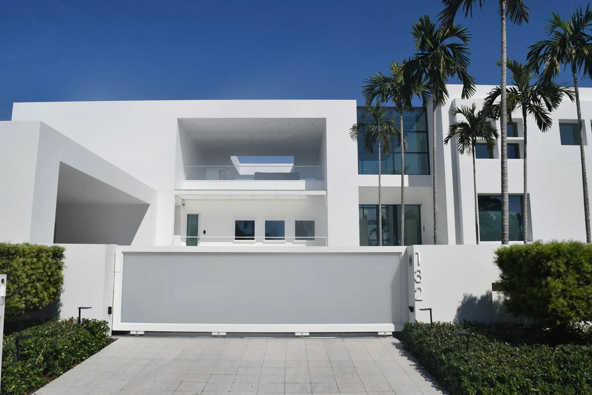 White house with large windows, clean lines, tropical landscaping, and gray front gate.