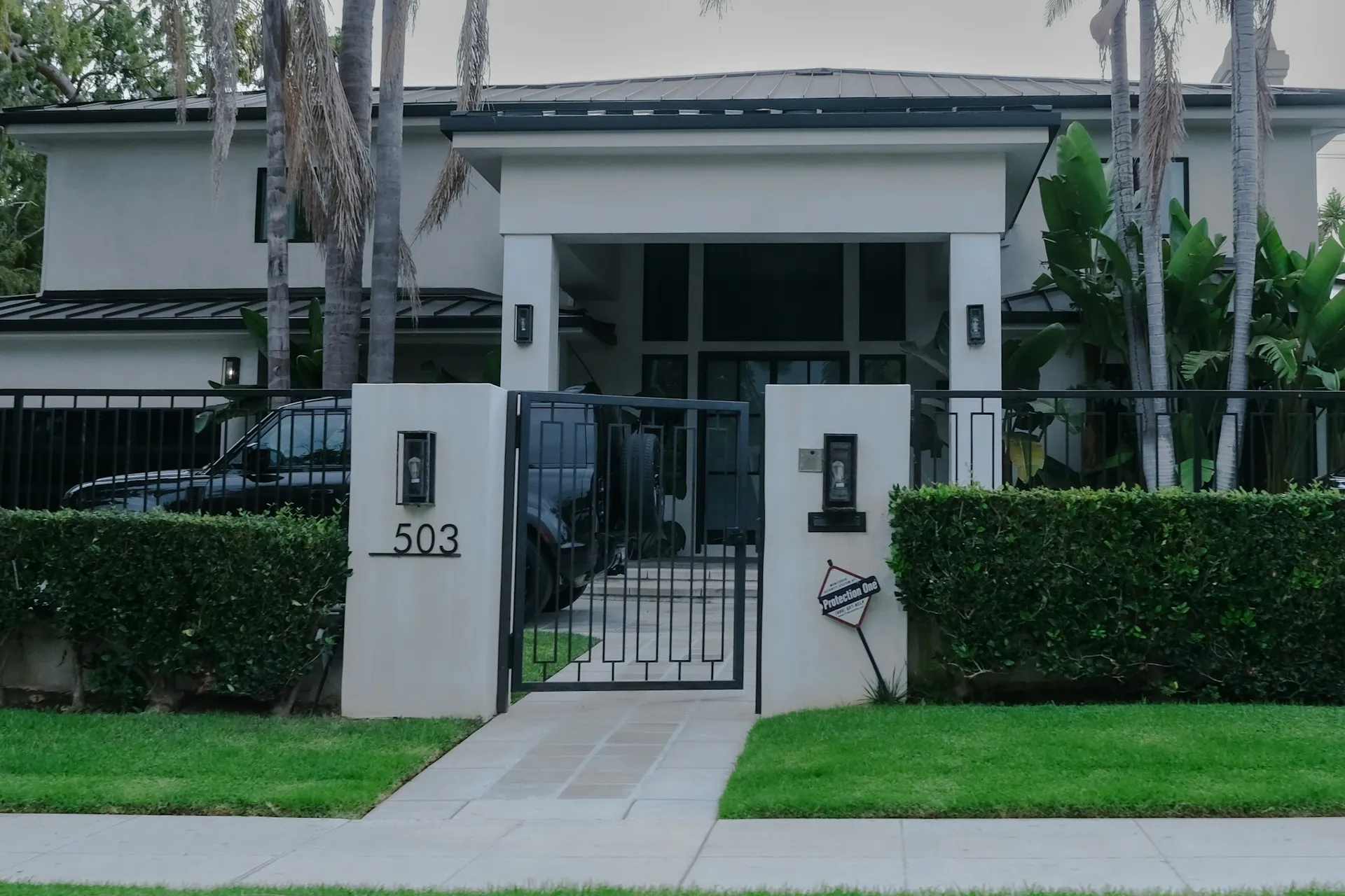 House California real estate with gate, yard, palm trees, and large windows.