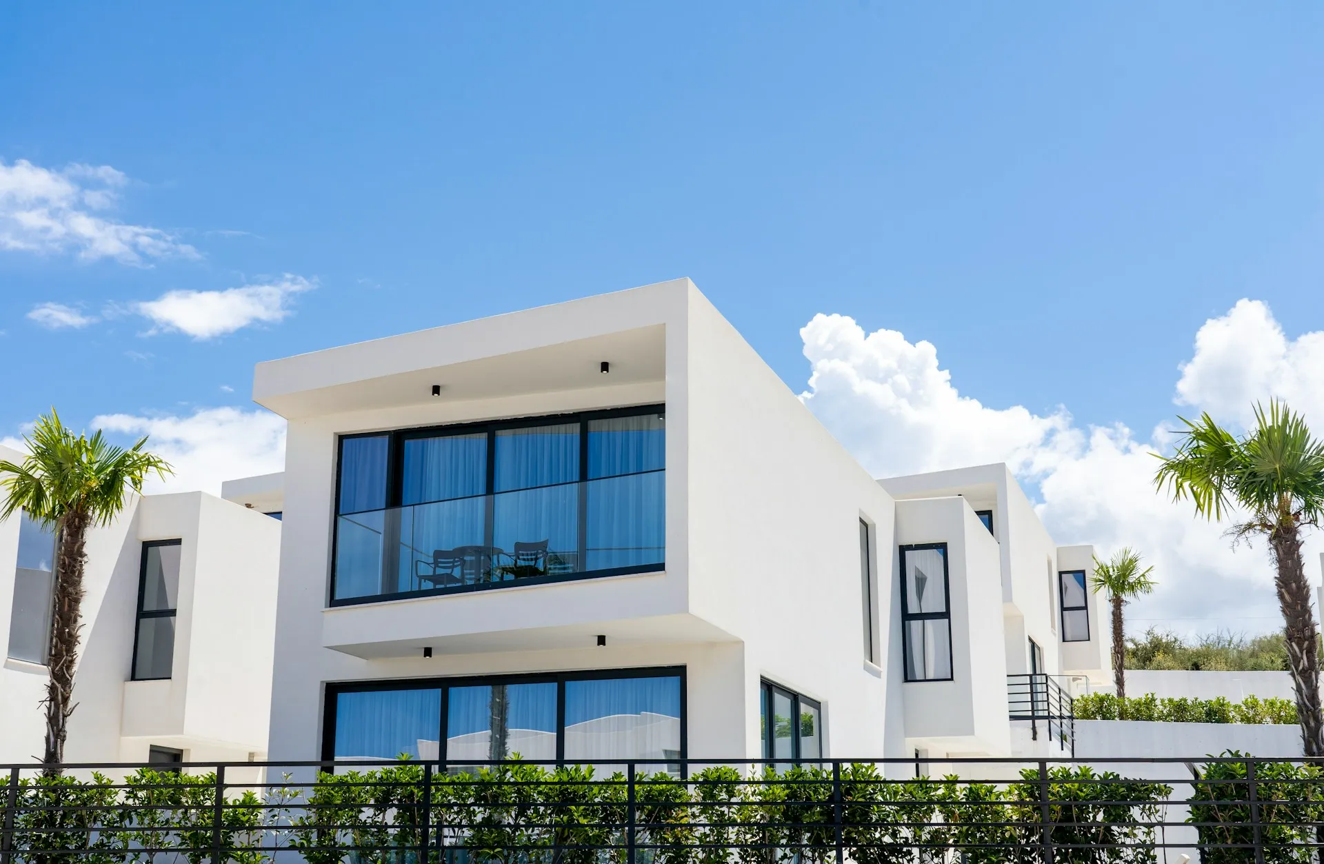 White house California real estate with large windows, balcony, and palm trees.